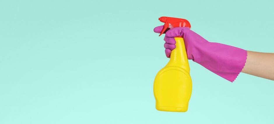 Mão com luva segurando um produto de limpeza para higienização das superfícies durante o isolamento domiciliar.