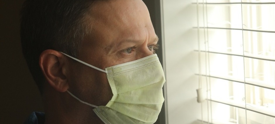 Homem vestindo máscara cirúrgica olhando pela janela